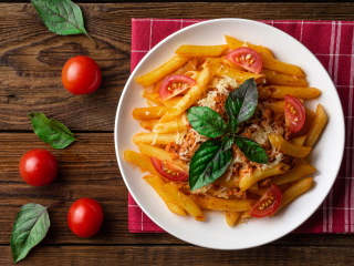 A Plate Of Pasta With Tomatoes And Basil On A Wooden Surface